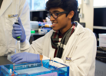 SF BUILD scholar in a white coat using a pipette.