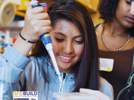 An SF BUILD scholar holding a pipette to put substance in a petri dish while a peer observes.