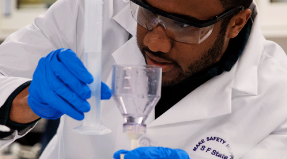 A student holding transferring liquid from a test tube to a flask.